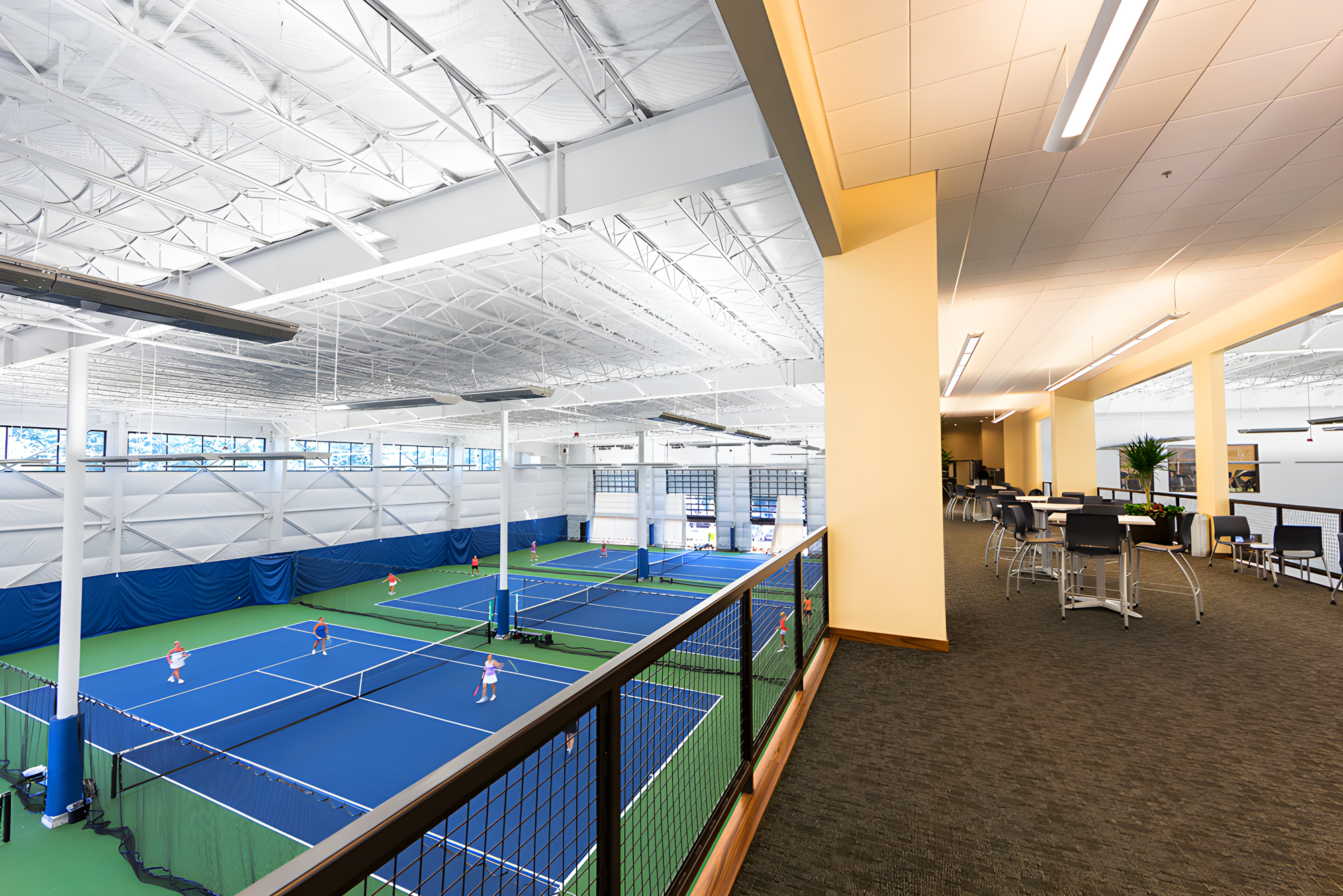 mezzanine view of indoor tennis courts with exposed steel ceiling and adjacent lounge seating